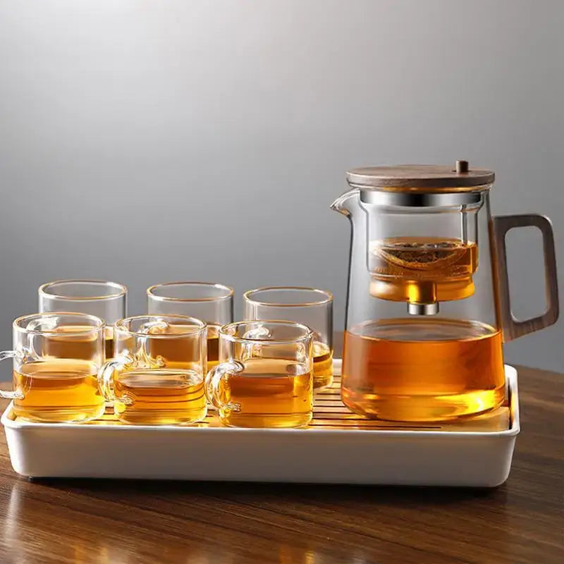 Elegant glass teapot with removable infuser and six tea cups on a wooden tray, showcasing brewed tea.