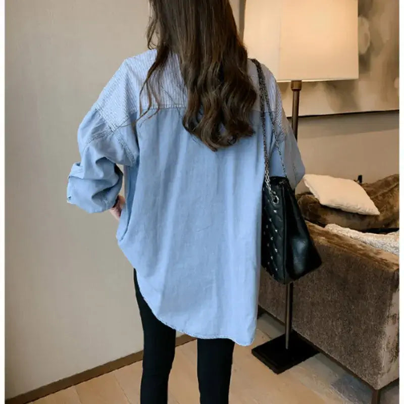 Back view of a loose fit women's denim shirt in light blue, styled casually with a black handbag.