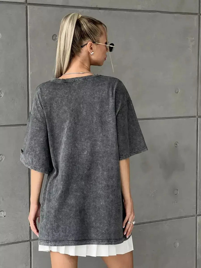 Back view of a model wearing a vintage-style dark grey oversized cotton t-shirt against a concrete wall.