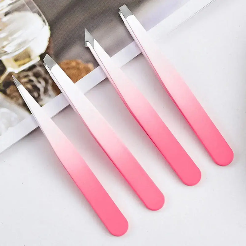 Set of four pink stainless steel eyebrow tweezers with flat and slant tips on a table.