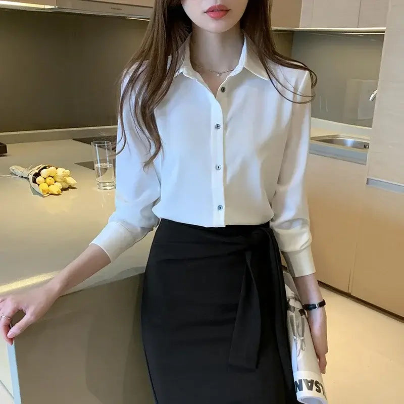 Woman wearing a white satin long sleeve blouse paired with a black skirt in a modern kitchen.