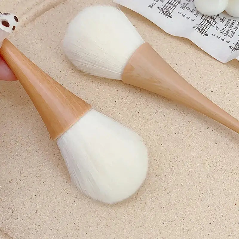 Two soft makeup brushes with wooden handles, perfect for dusting nail residue and applying loose powder.