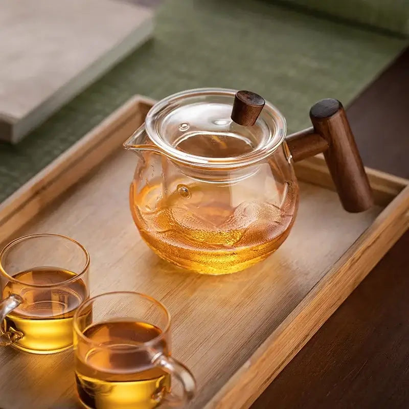 450ml heat-resistant glass teapot with wooden handle and infuser, placed on a tray with two tea cups.