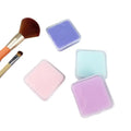 Four colors of makeup brush cleaner soap with brushes on a white background