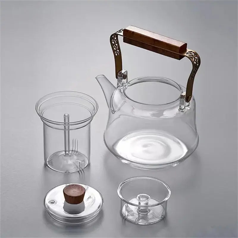 Japanese heat resistant glass teapot with copper wood handle and tea infuser components on gray background.