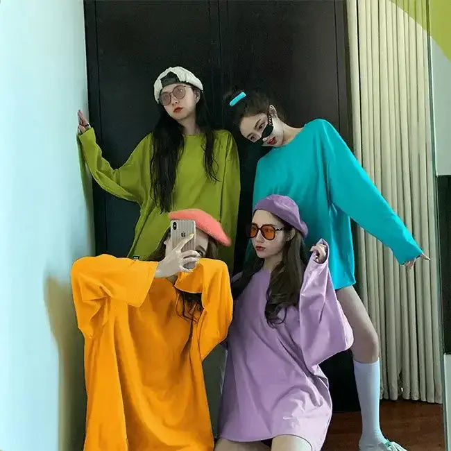 Group of young women in colorful long sleeve t-shirts and sunglasses posing for a photo, showcasing trendy spring fashion.