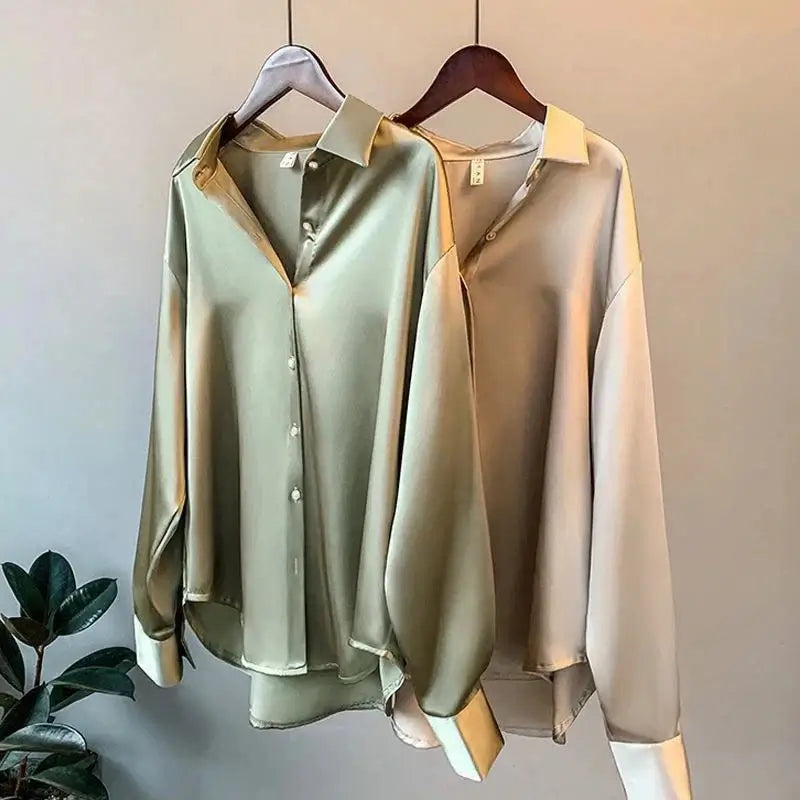 Two elegant satin long sleeve button-up shirts in green and beige hanging on display.