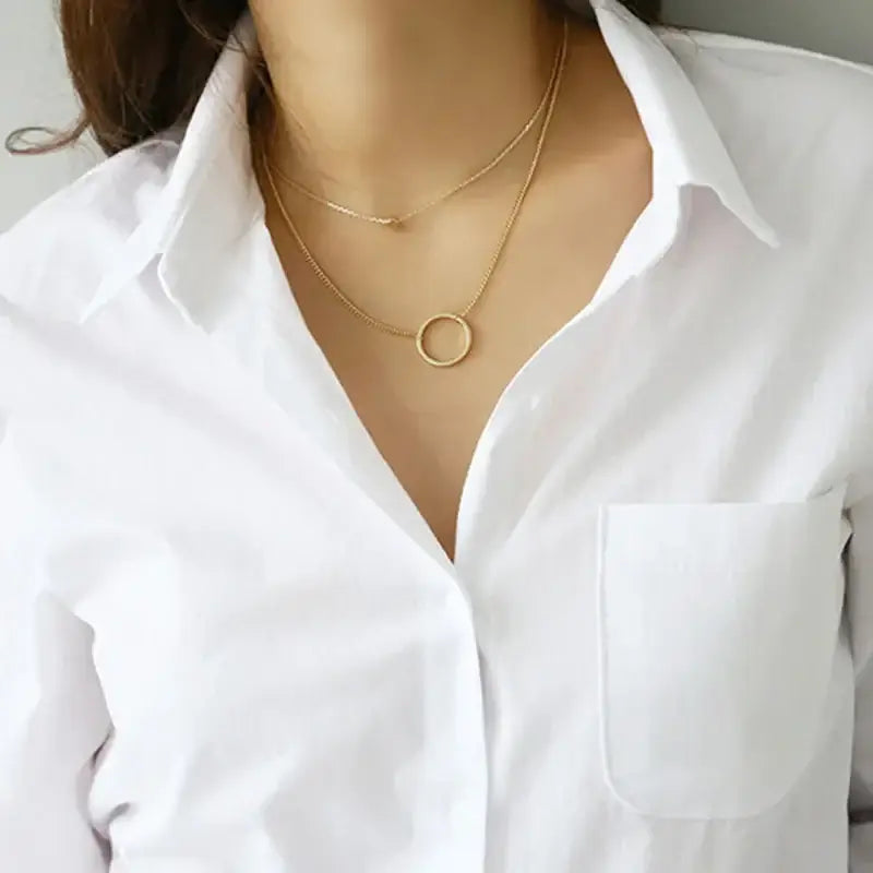 Close-up of a woman wearing a white blouse with a pocket and layered gold necklaces.