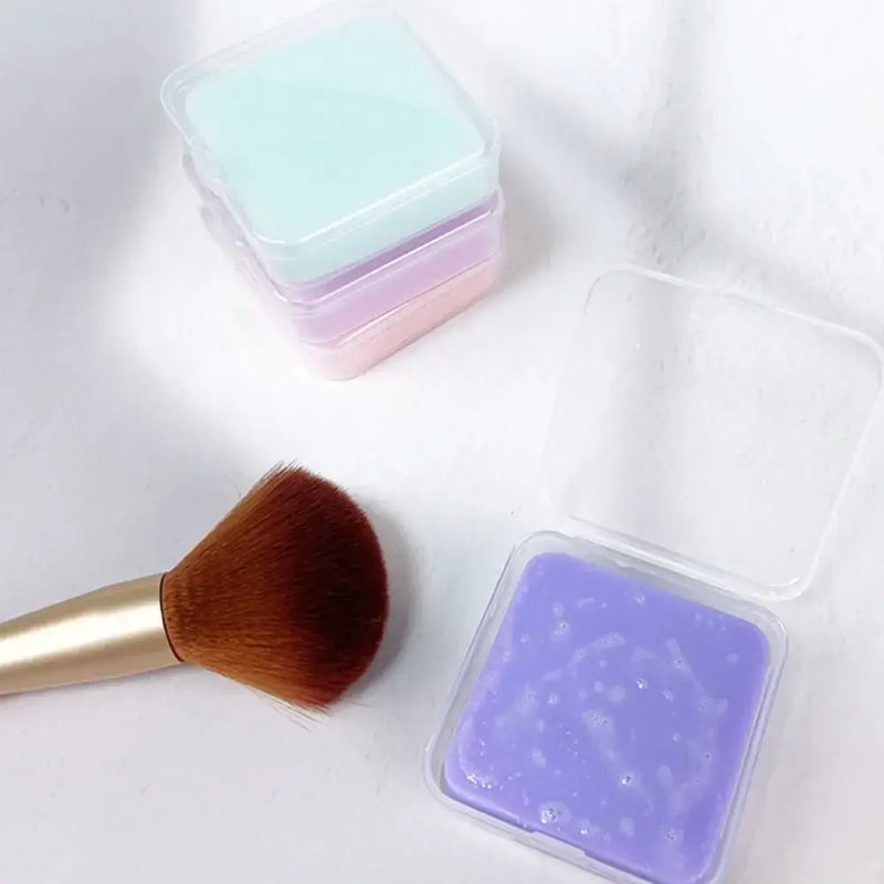 Colorful makeup brush cleaner soaps in containers with a makeup brush beside them.