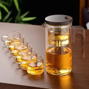 Heat-resistant glass teapot with stainless steel infuser and tea cups, beautifully showcasing brewed tea.