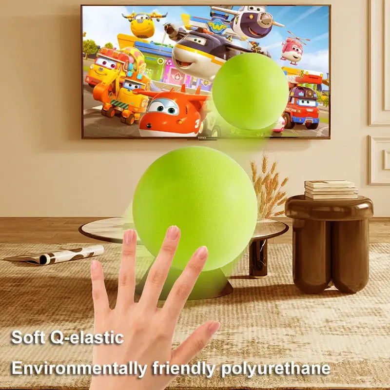 Child's hand reaching for soft green elastic ball in playroom with animated show on TV.