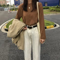 Woman in a brown long sleeve top, white jeans, and beige jacket, walking in a casual outdoor setting.