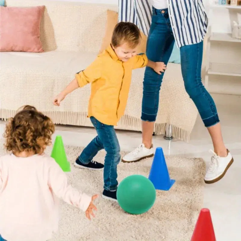 Children playing with colorful cones and a green ball indoors, enjoying fun and active games on a carpet.