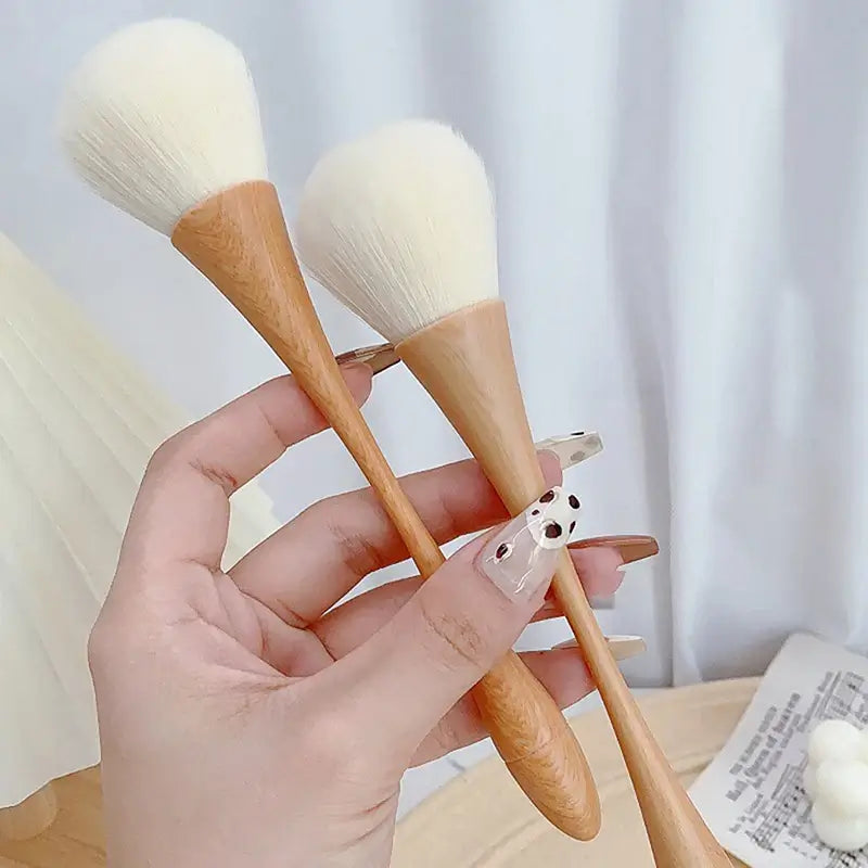 Hand holding three eco-friendly dust cleaning nail and makeup brushes with wooden handles on a table.