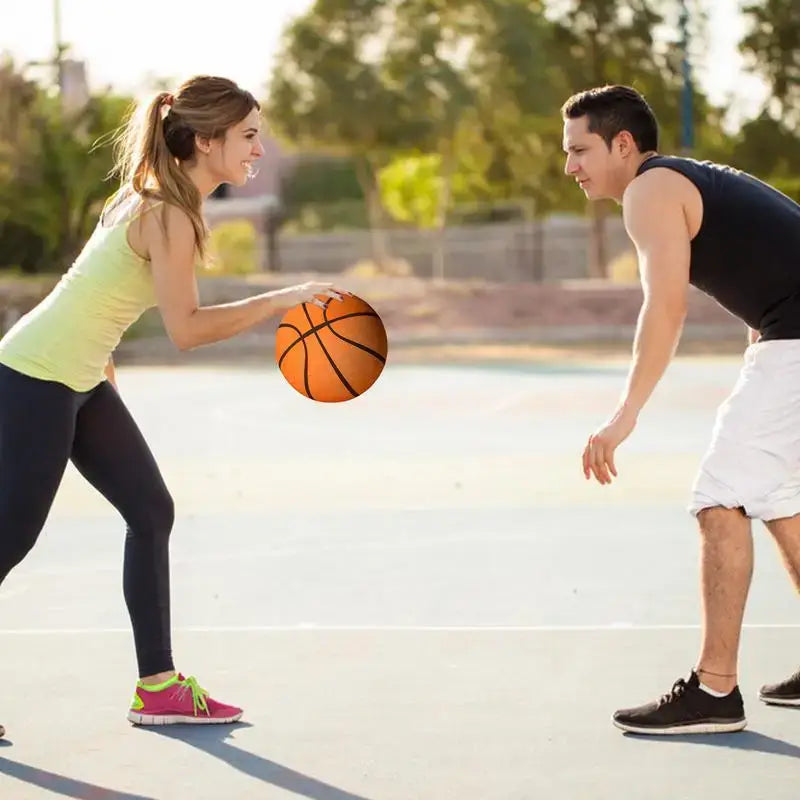 Two people playing basketball outdoors, one dribbling a basketball while the other defends.