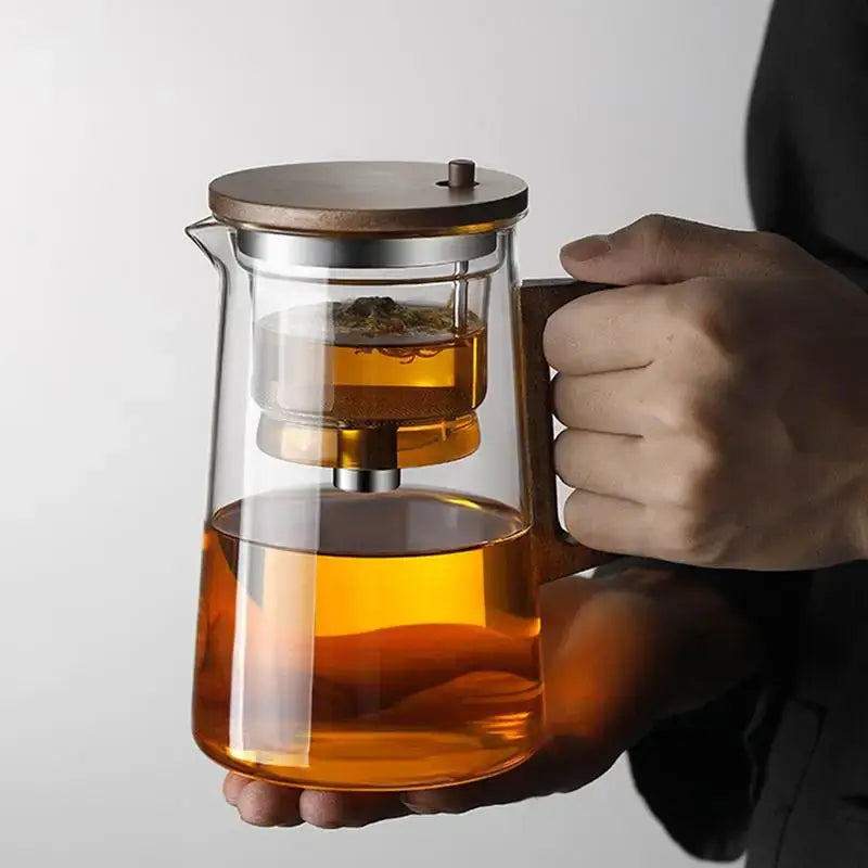 Glass teapot with removable infuser, holding hot tea, featuring a wooden lid and modern design.