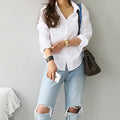 Elegant white blouse with turn-down collar, paired with ripped jeans for a casual office look.