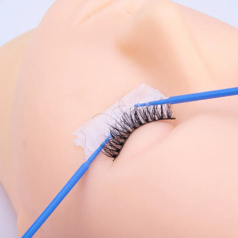 Eyelash extension application on silicone practice model with a blue wand and adhesive tape.