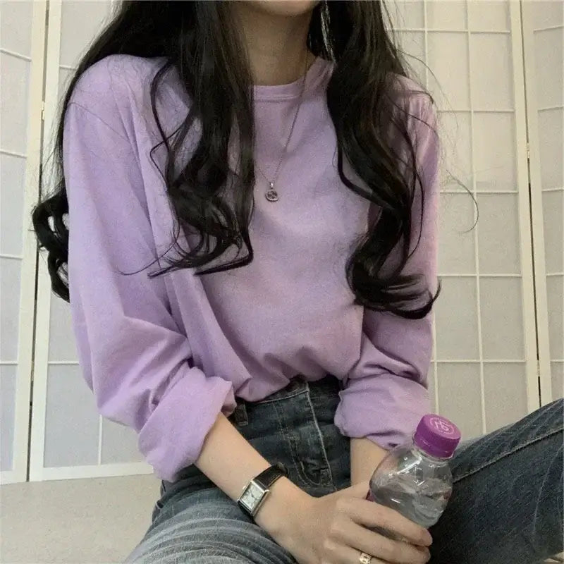 Woman in a loose-fit purple long sleeve T-shirt, casually holding a water bottle, showcasing a stylish outfit.