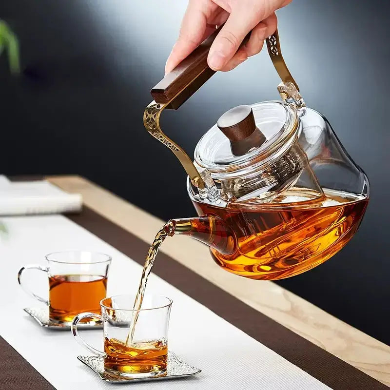 Japanese glass teapot with wood handle pouring tea into cups on a table, showcasing its elegant design and functionality.