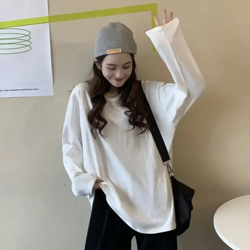 Woman in white long sleeve loose-fit T-shirt with crew neck and beanie, showcasing trendy spring fashion.