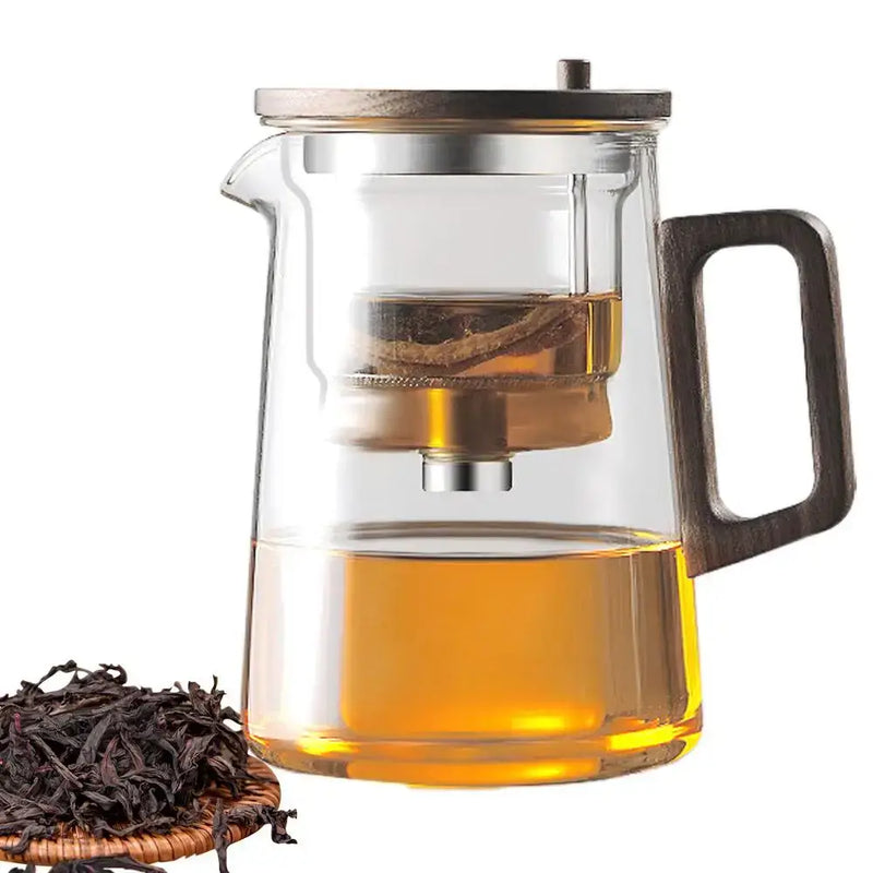 Glass teapot with removable infuser, showcasing brewed tea and dry leaves on a wooden plate.