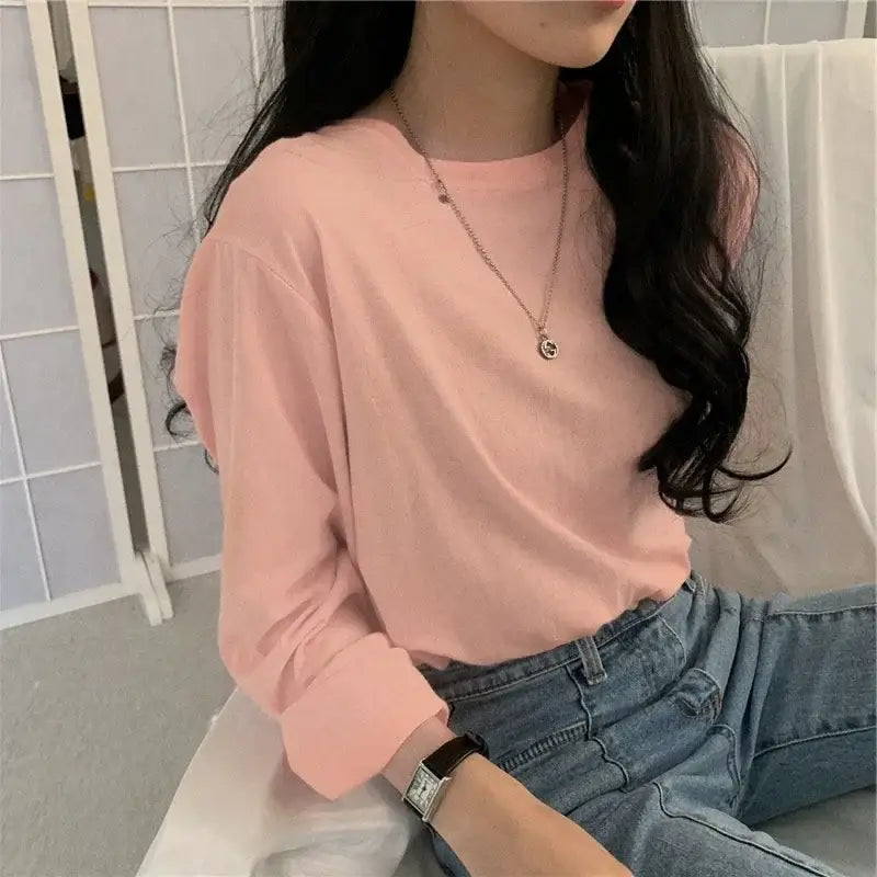 Woman wearing a pink long sleeve loose-fit T-shirt, styled with jeans and accessories, showcasing a casual look.