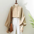 Stylish women's blouse in beige with long lantern sleeves and stand collar, paired with white trousers and a brown bag.